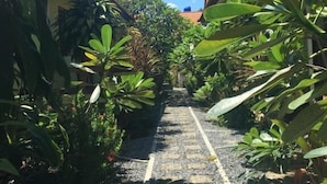 A narrow pathway flanked by lush greenery and a building with a tiled roof. - Baan Promjan (Koh Samui)