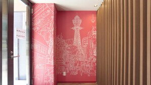 A hallway with a red wall featuring a white cityscape mural, a wooden slat wall on the right, and a glass door on the left. - Hotel Zipang (Osaka)