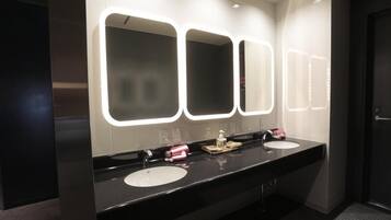 Une salle de bain moderne avec deux vasques, un grand miroir dont les bords sont éclairés, et un porte-serviettes.