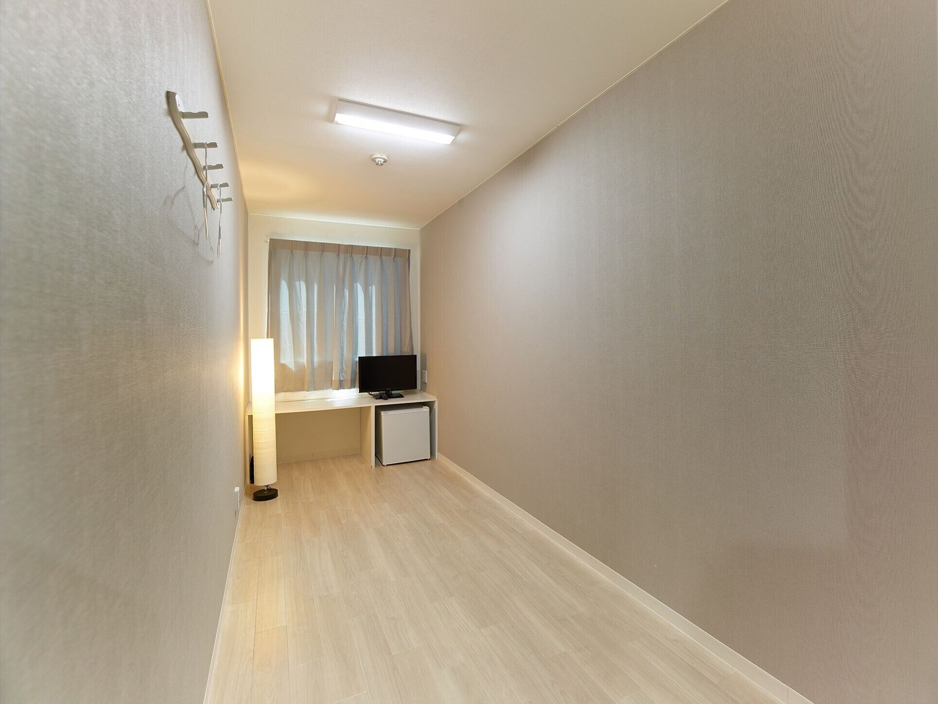 A narrow hallway with a desk, a television, and a small refrigerator.