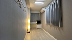 A narrow hallway with a wooden floor, a wall-mounted coat rack, a ceiling light, and a window with curtains. - Hotel Zipang (Osaka)