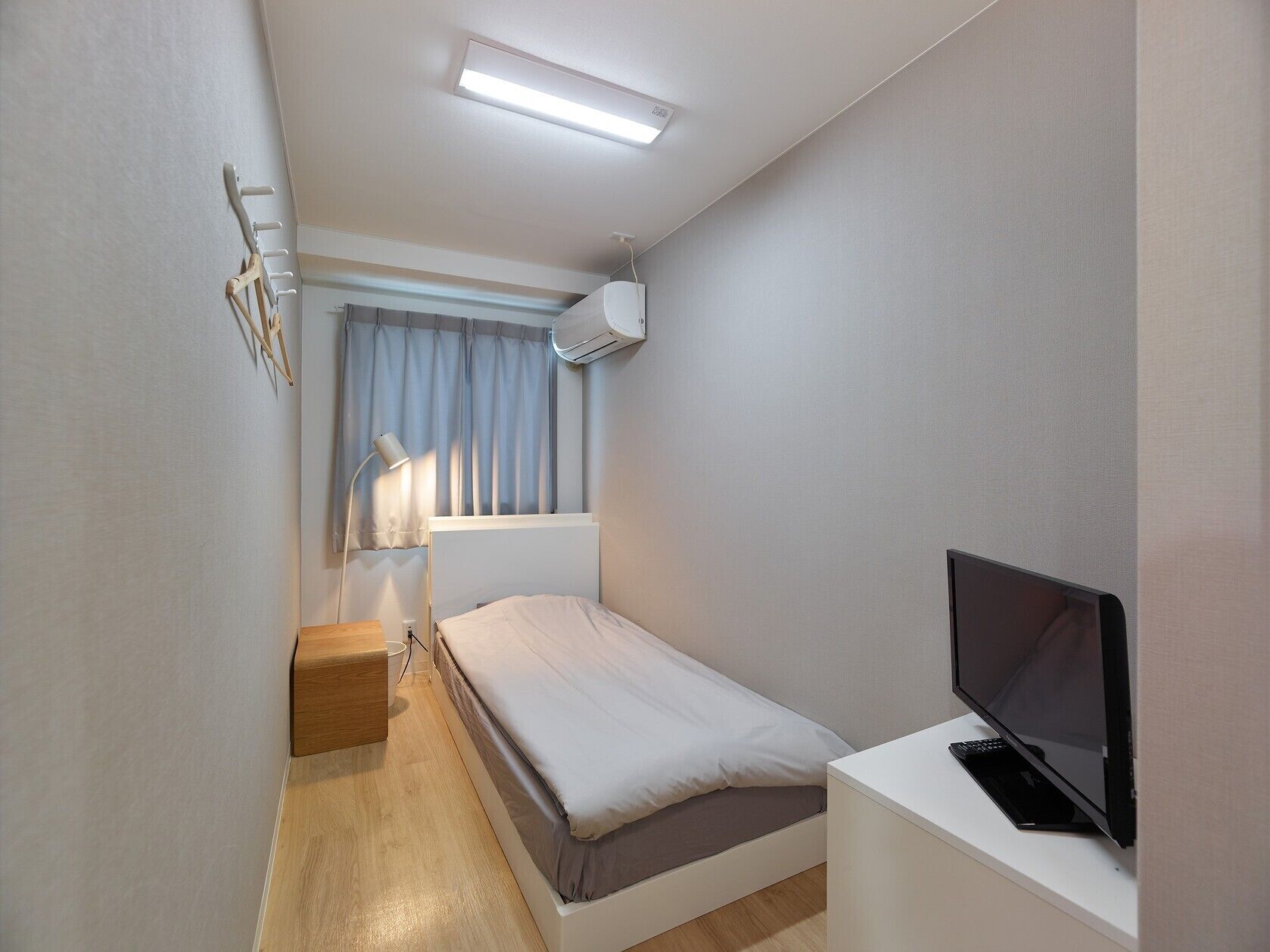 A small, modern bedroom with a bed, bedside table, TV, and an air conditioning unit.