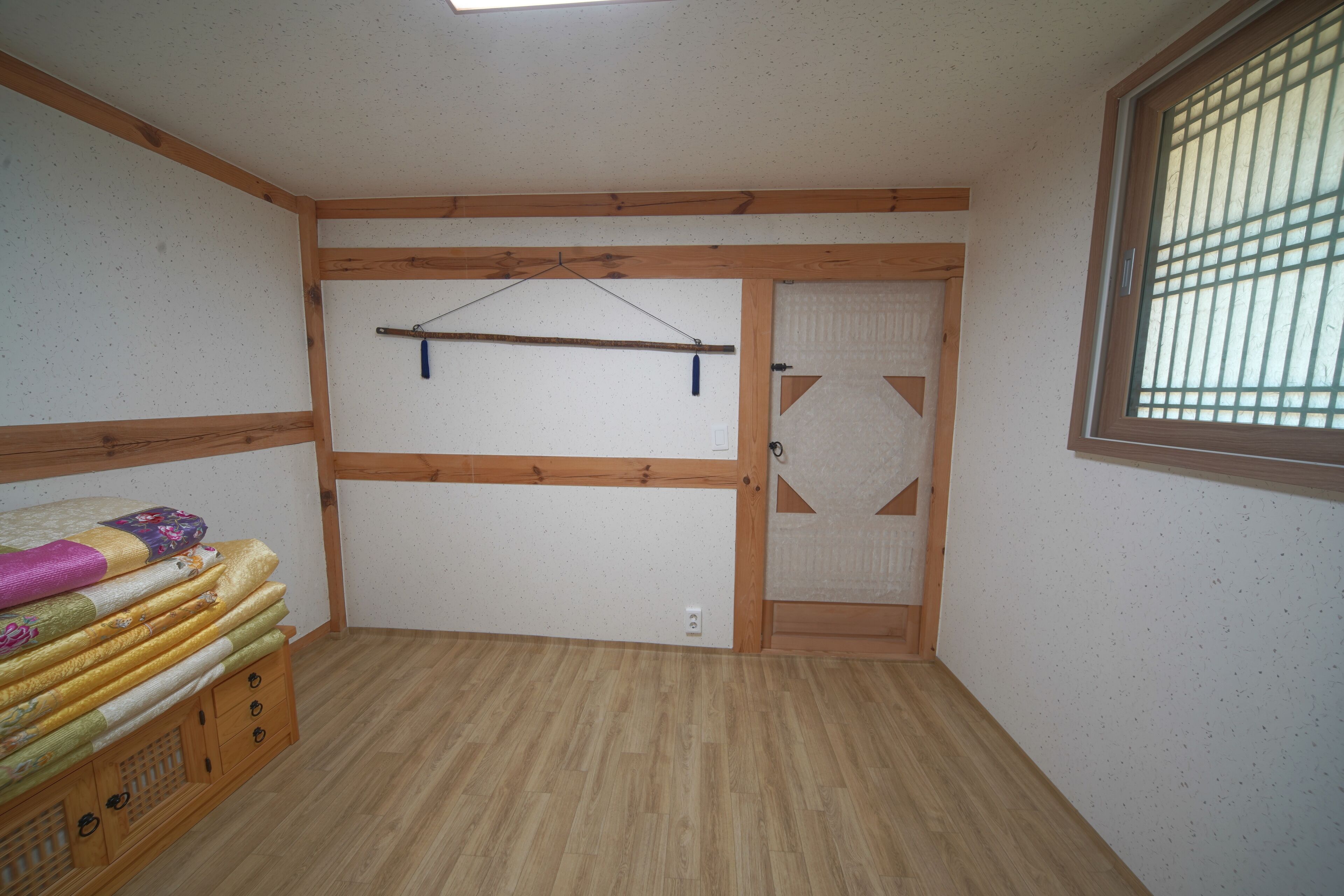 Una habitación con piso de madera, una cama con cabecera, un armario con puerta corredera y una ventana con rejas.