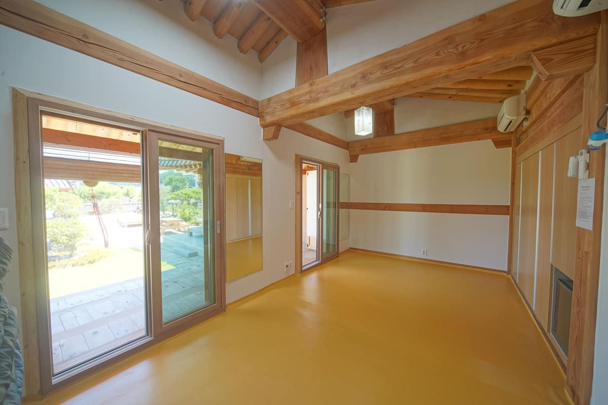A spacious room with wooden beams, large sliding glass doors, and a bright yellow floor.