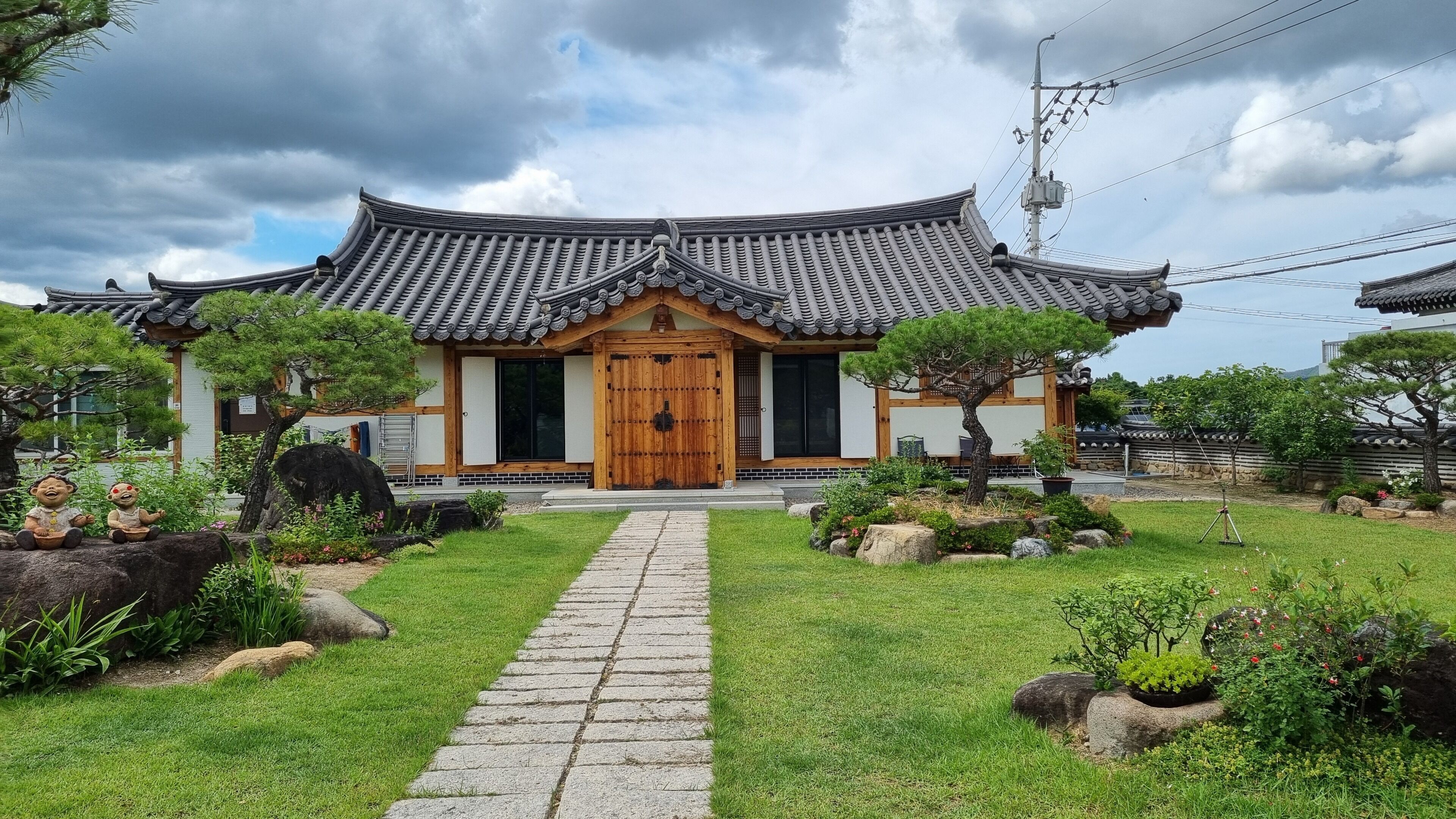 Un edificio in stile coreano tradizionale con tetto in tegole, ingresso in legno e un giardino curato con rocce e piante.