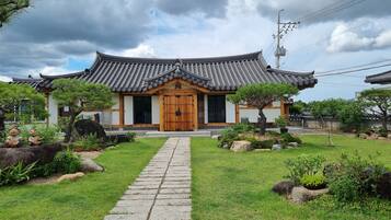 Un edificio in stile coreano tradizionale con tetto in tegole, ingresso in legno e un giardino curato con rocce e piante.