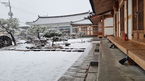 A traditional building with a wooden exterior and tiled roof, a stone pathway, and a snow-covered garden.