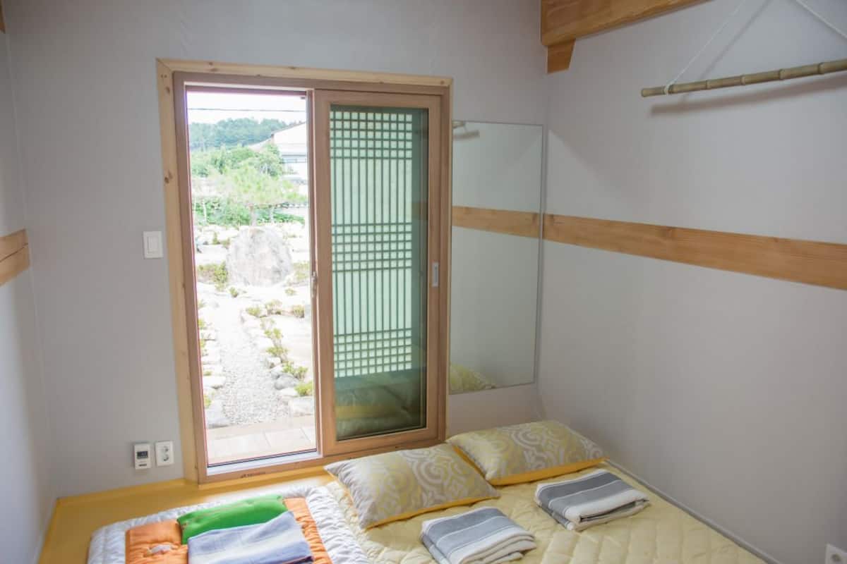 A small room with a bed, a sliding door to a balcony, and a wooden beam on the ceiling.