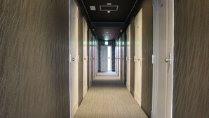 A hotel corridor with carpeted floors and wooden panel walls, leading to a bright room at the end.