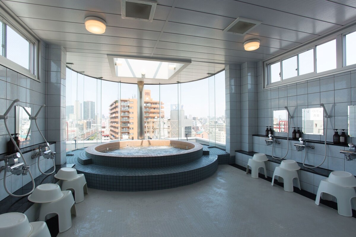 A modern bathroom with a central hot tub, large windows, and a city view.