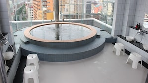 A modern bathroom with a circular hot tub, white stools, and a view of the city through large windows.