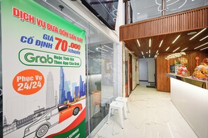 A hotel interior with a reception desk, a promotional poster advertising Grab service, and a view of the cityscape through the window. - Yoko Airport Saigon Hotel (Ho Chi Minh City)