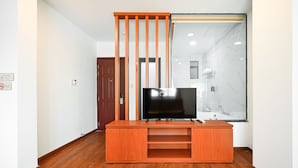 A modern living room with a wooden entertainment unit, a flat-screen TV, and a glass shower enclosure. - Yoko Airport Saigon Hotel (Ho Chi Minh City)