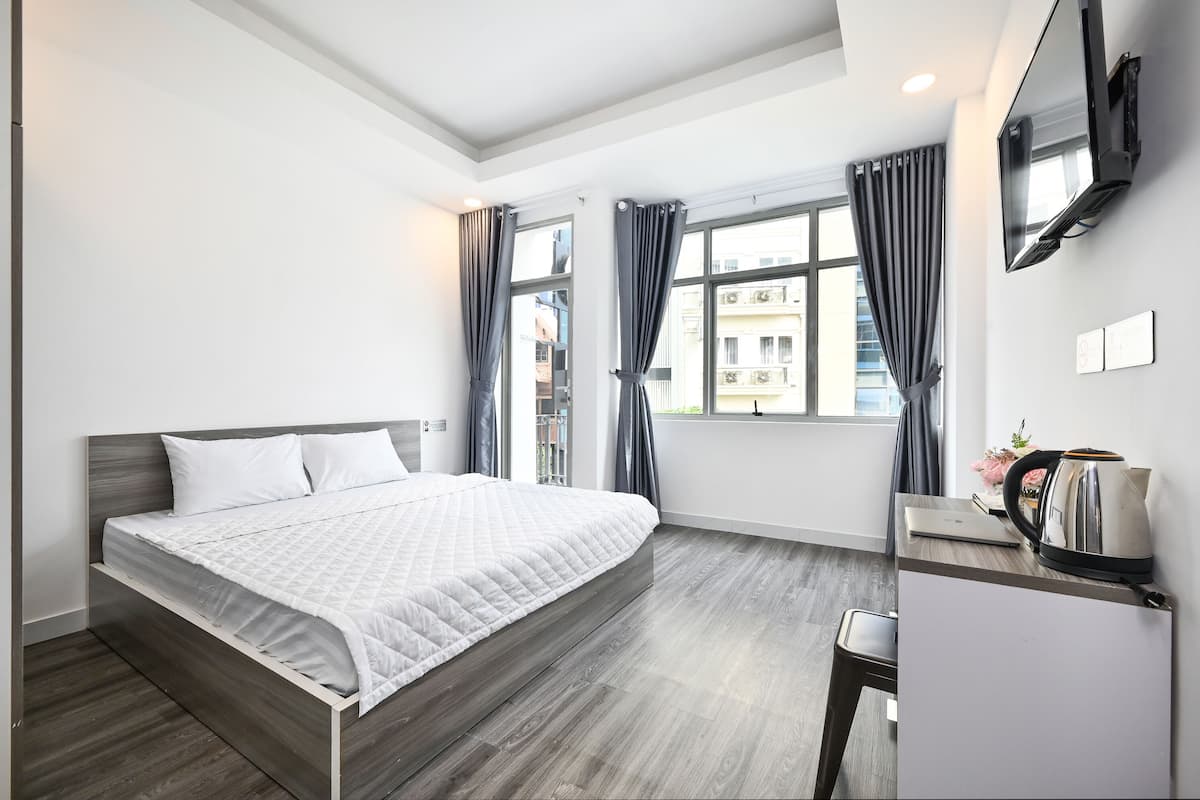 Habitación de hotel moderna con una cama, un escritorio con una computadora portátil, una tetera y un televisor en la pared.