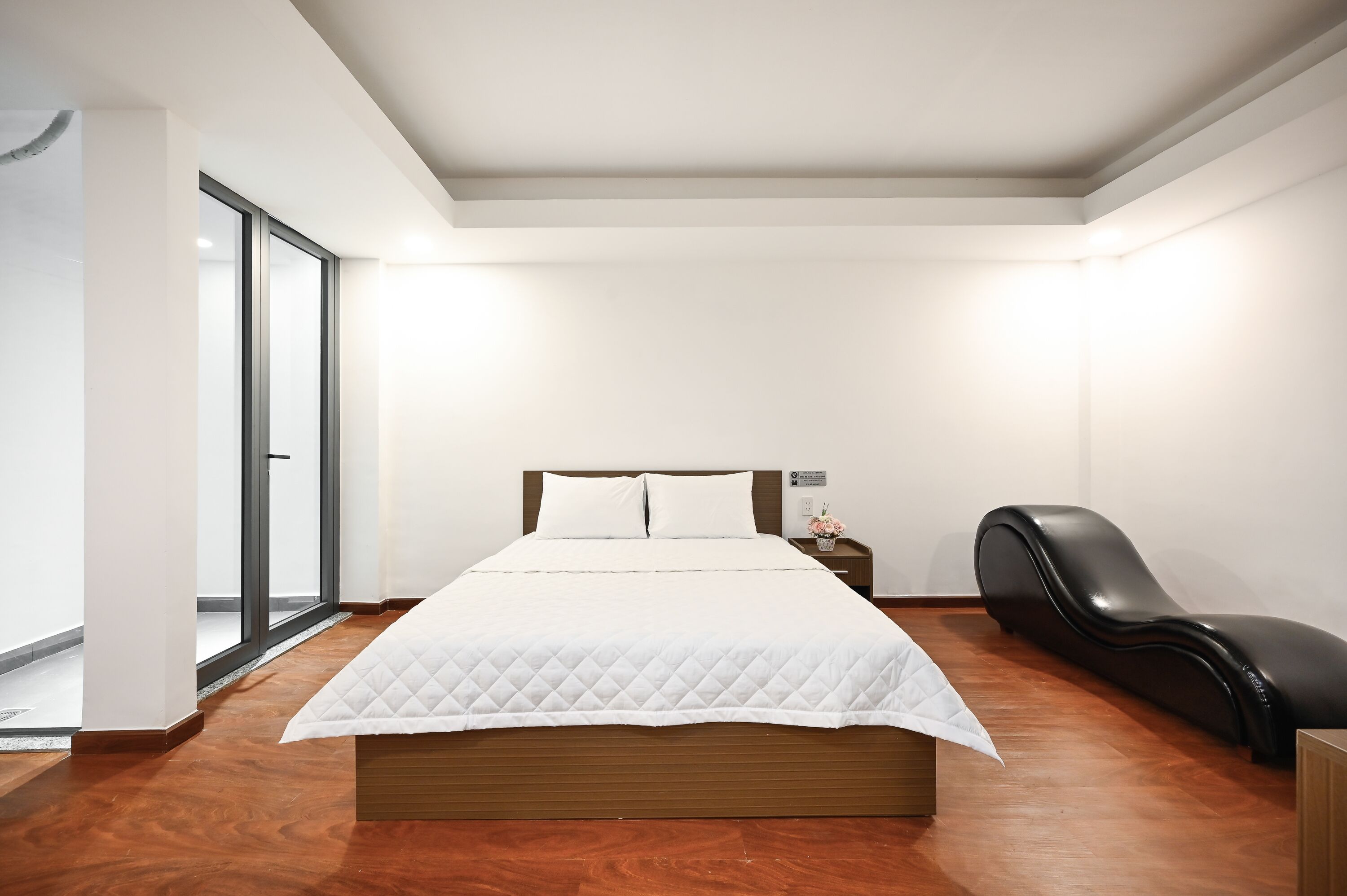 A modern bedroom with a wooden bed, a black leather chair, and a large window.
