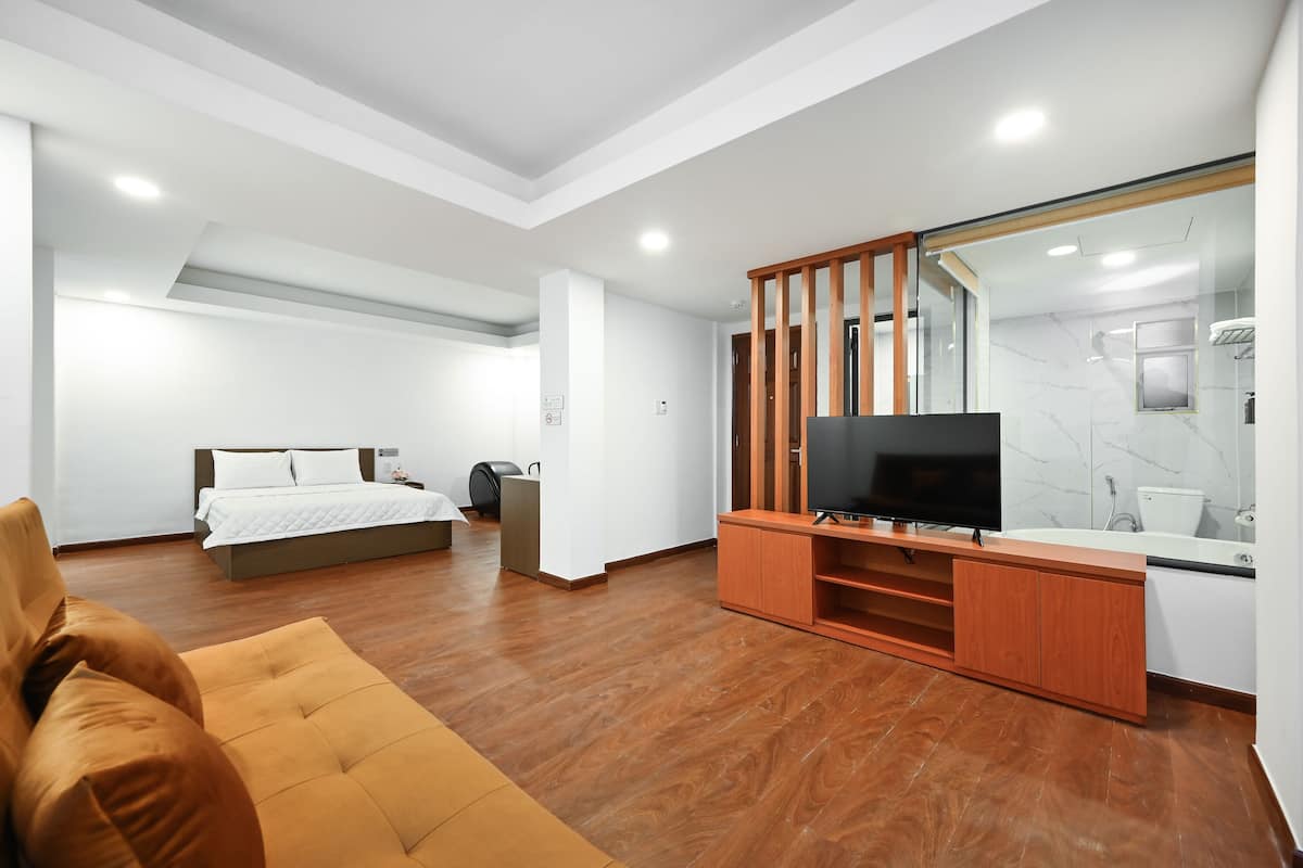 Una habitación de hotel moderna con una cama, un televisor, un armario de madera y un baño con espejo y lavamanos.
