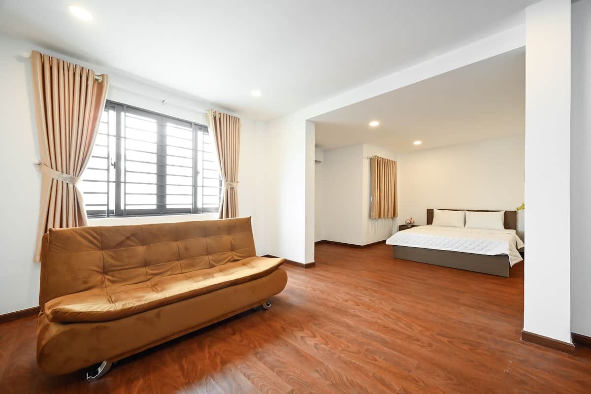 Una habitación amplia con sofá, cama y un ventanal con cortinas.