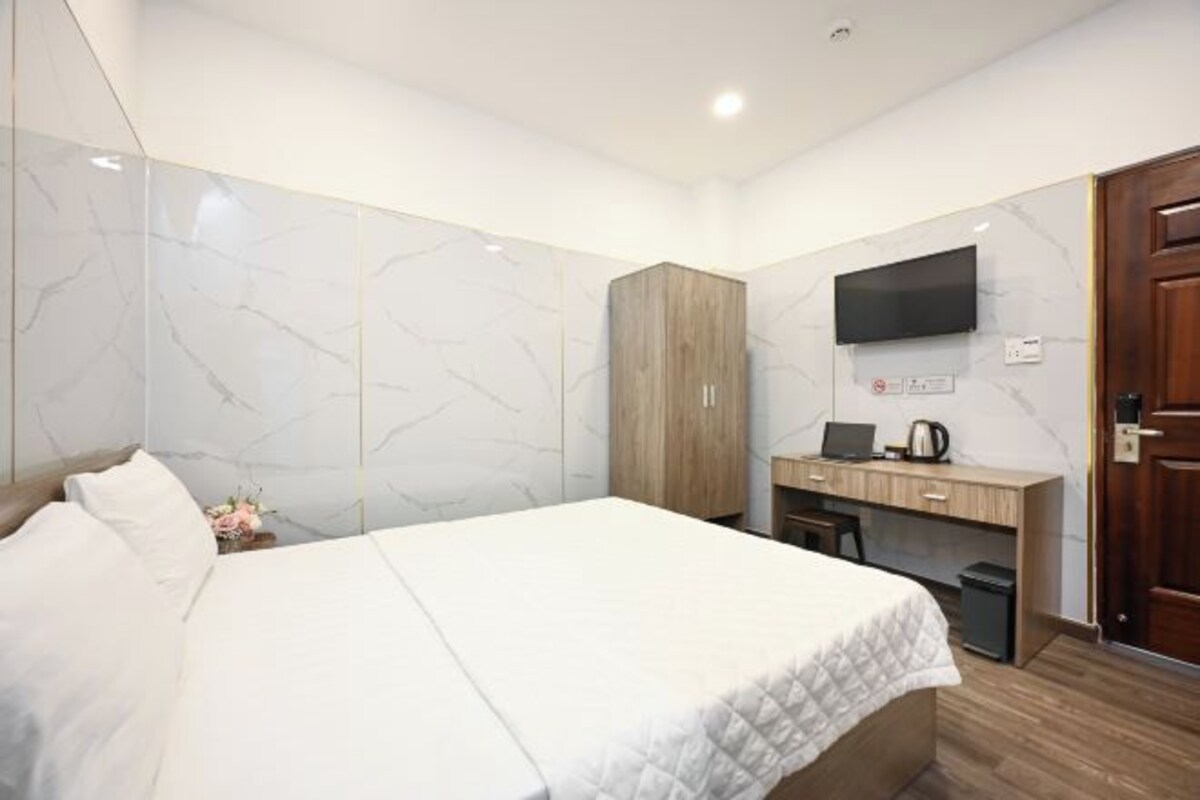 Une chambre d’hôtel avec un grand lit, une armoire en bois, un bureau avec un ordinateur portable, un téléviseur à écran plat et une porte en bois.