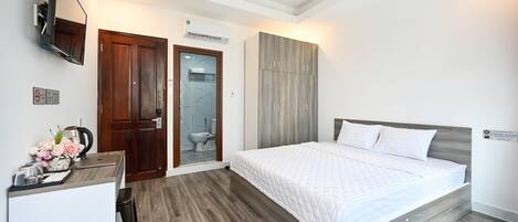 A bedroom with a bed, a desk with a chair, a TV mounted on the wall, and a wardrobe.
