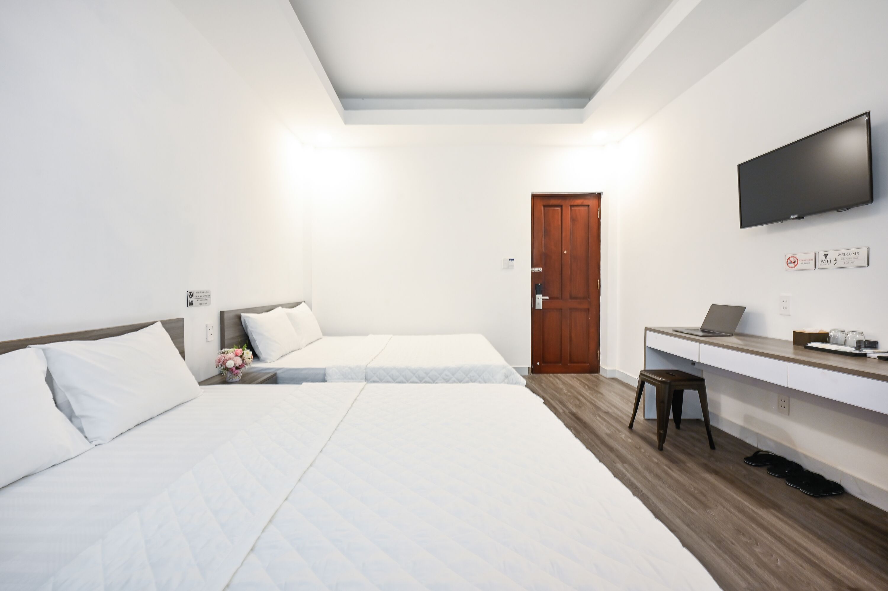 Ein Hotelzimmer mit zwei Betten, einem Schreibtisch mit einem Laptop, einem Fernseher und Holzboden.