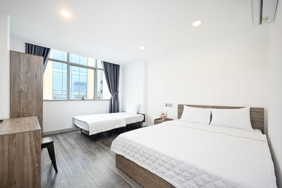 Una habitación de hotel con una cama grande, otra más pequeña, un escritorio y una ventana con cortinas.