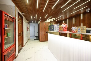 A hotel reception area with a Coca-Cola vending machine, a wooden reception desk, and a sign for the Yoko Airport Hotel. - Yoko Airport Saigon Hotel (Ho Chi Minh City)