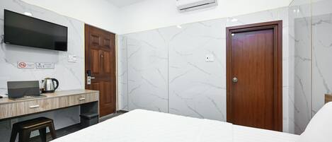 A hotel room with a bed, a desk with a laptop and a coffee maker, a TV mounted on the wall, and marble-patterned walls.