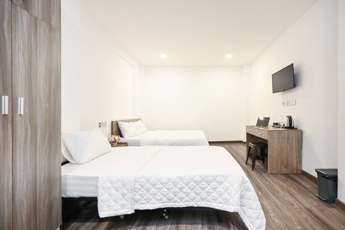Una habitación de hotel con dos camas, un escritorio, un televisor y un cubo de basura.