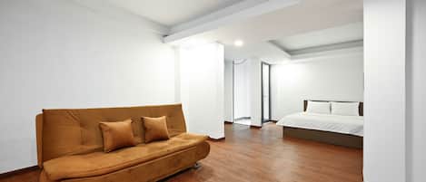 A modern, empty room with a brown sofa, a bed, and wooden flooring.