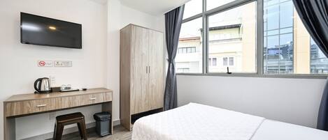 A hotel room with a bed, a desk, a TV, and a window with curtains.