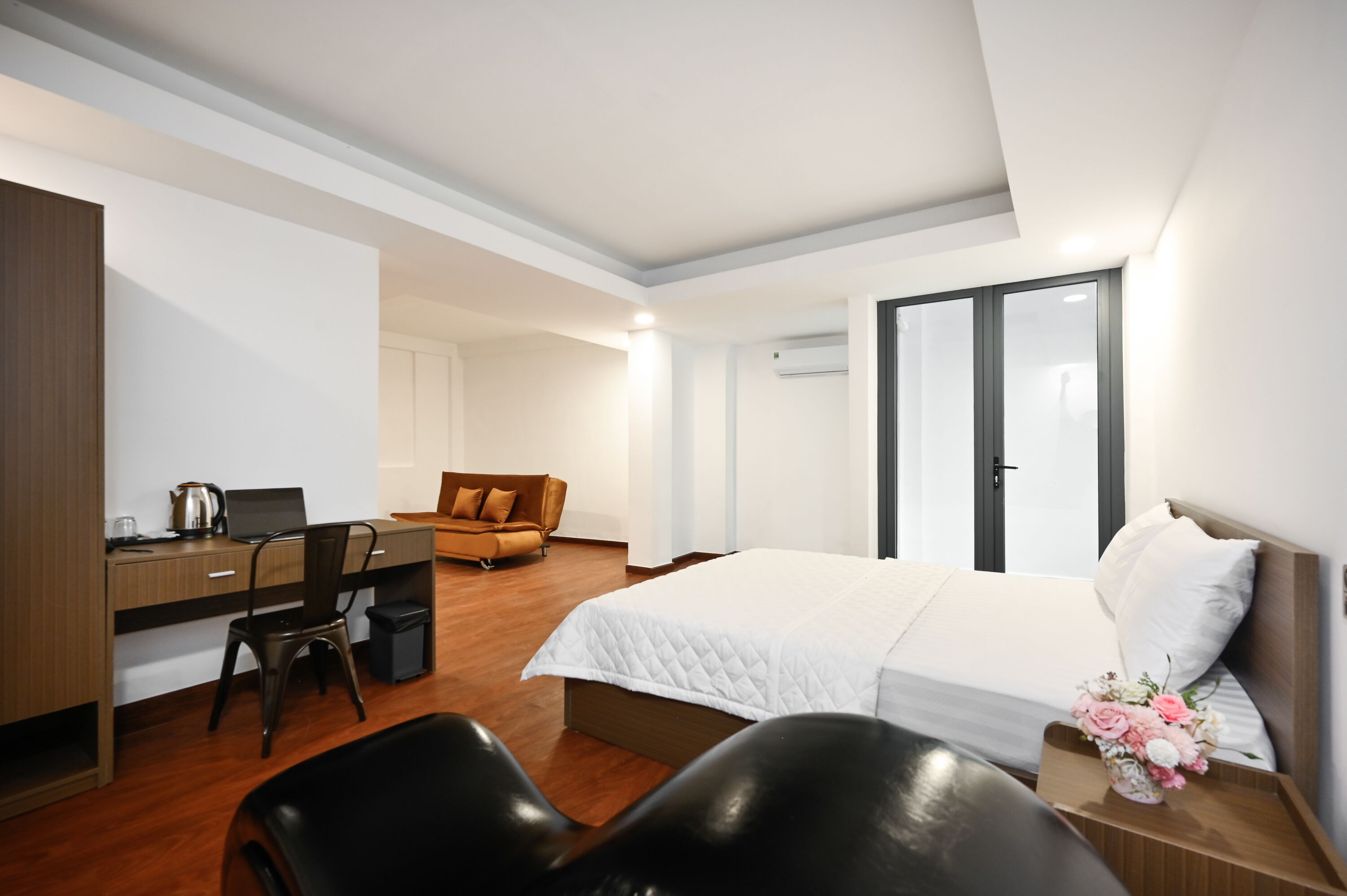 A modern hotel room with a bed, desk, chair, and a sofa.