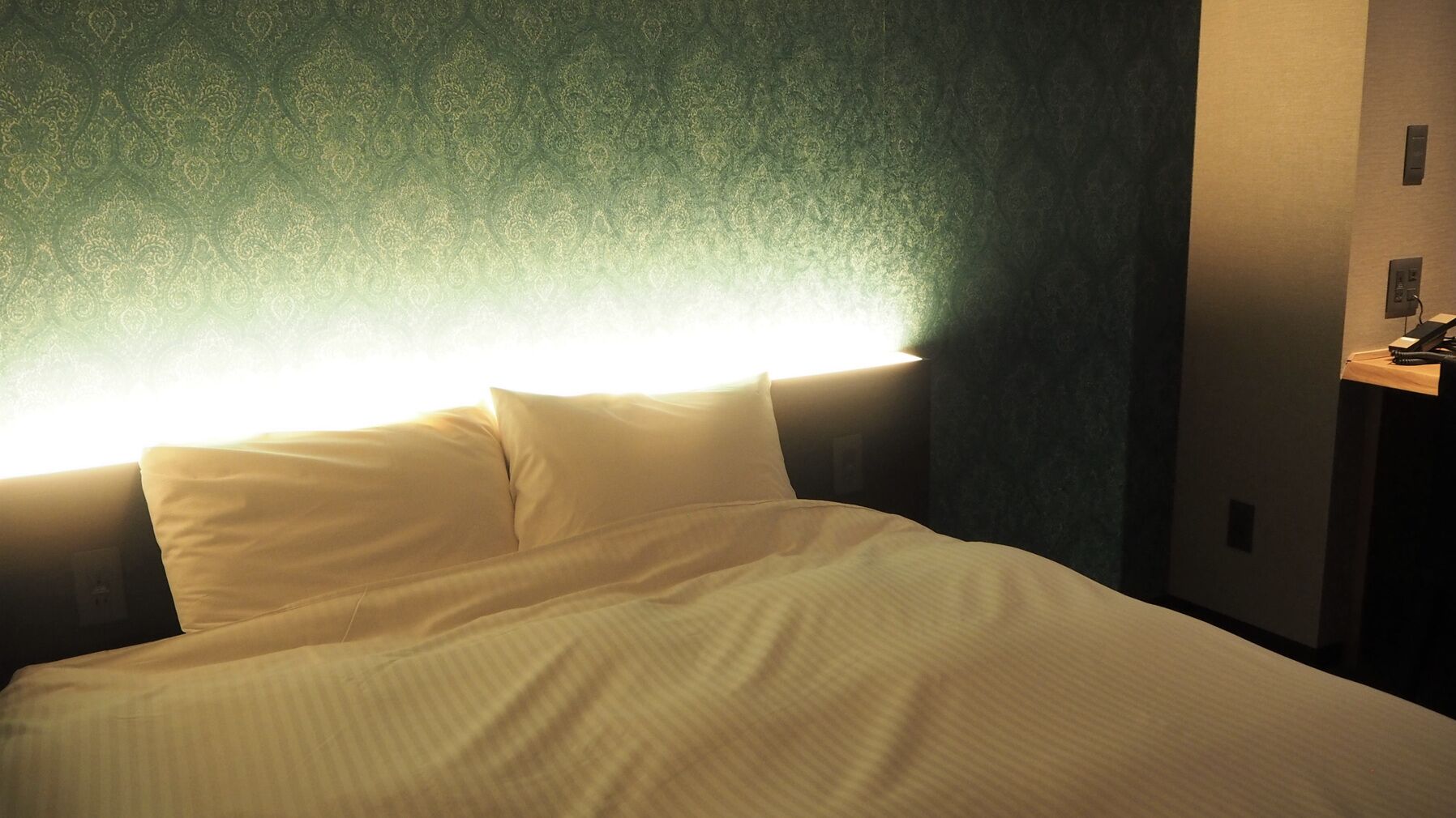 Een bed met witte lakens, een hoofdbord en een muur met behang met een patroon.