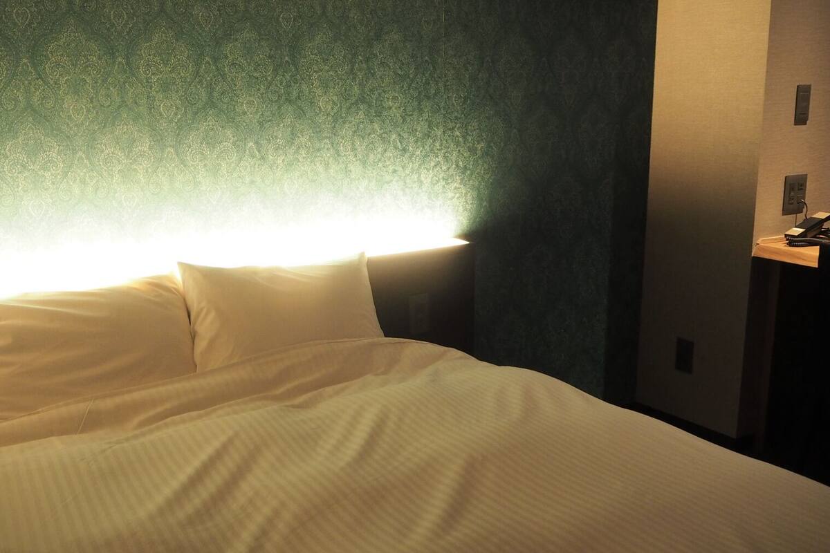 Een bed met witte lakens, een hoofdbord en een muur met behang met een patroon.