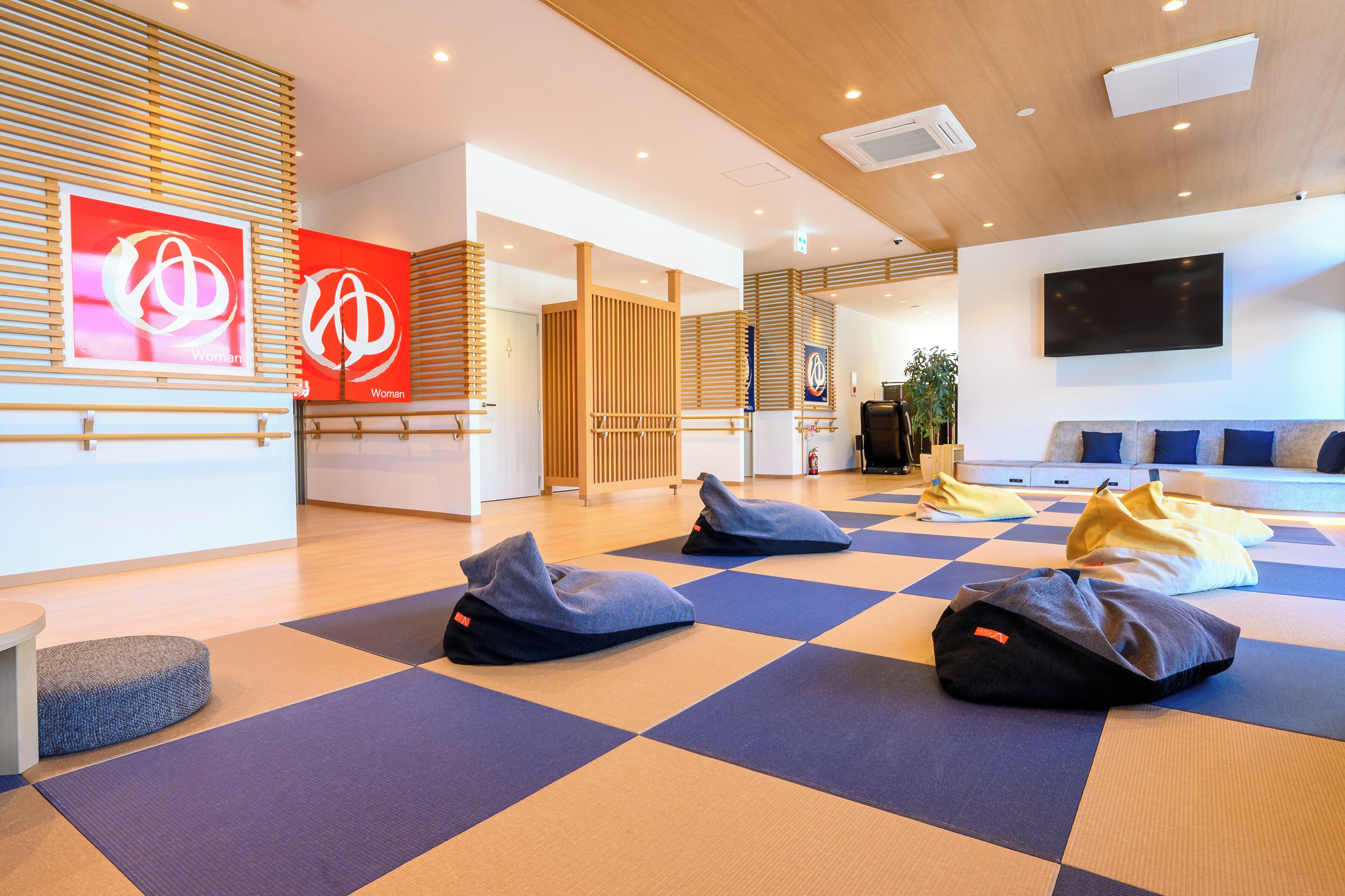 A modern hotel lobby with a checkered floor, seating areas, and a large TV screen.