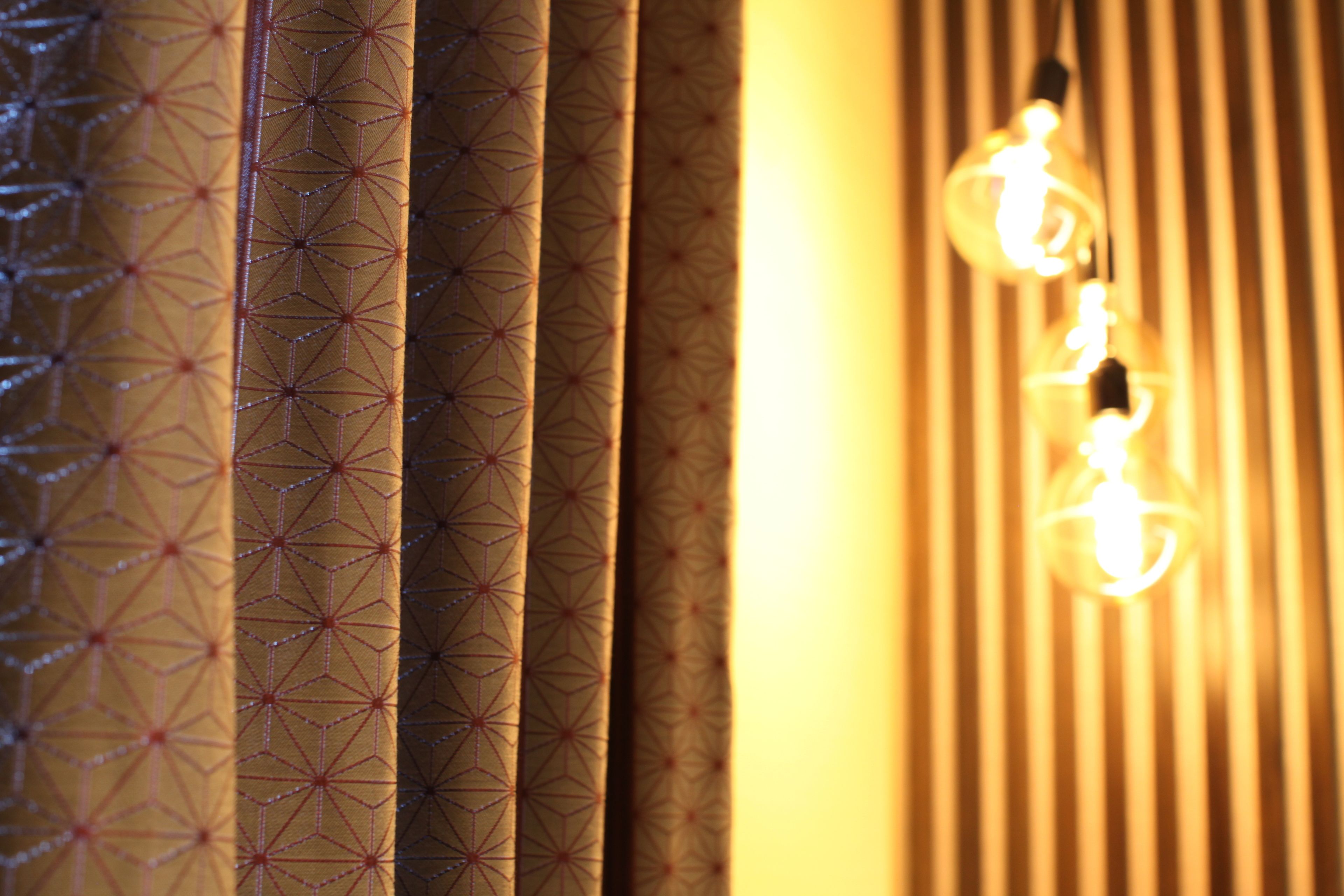 A close-up of patterned curtains and hanging light bulbs.