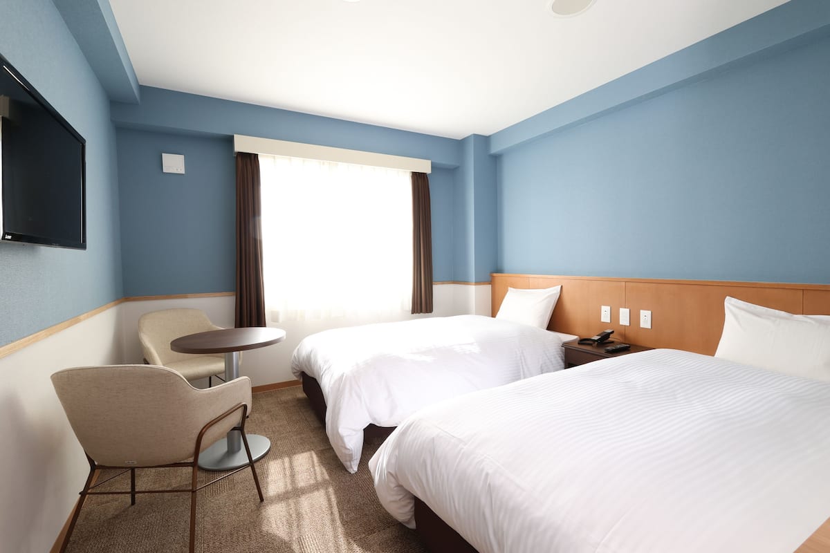 Une chambre d’hôtel avec deux lits, un bureau, une chaise, une télévision et une fenêtre avec des rideaux.