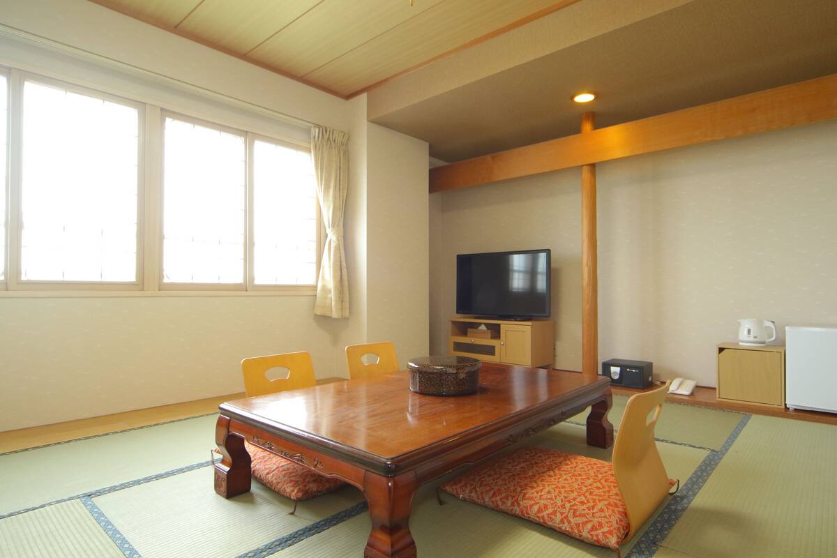 Une pièce de style japonais traditionnel, avec un sol recouvert de tatamis, une table basse et un téléviseur posé sur un meuble en bois.