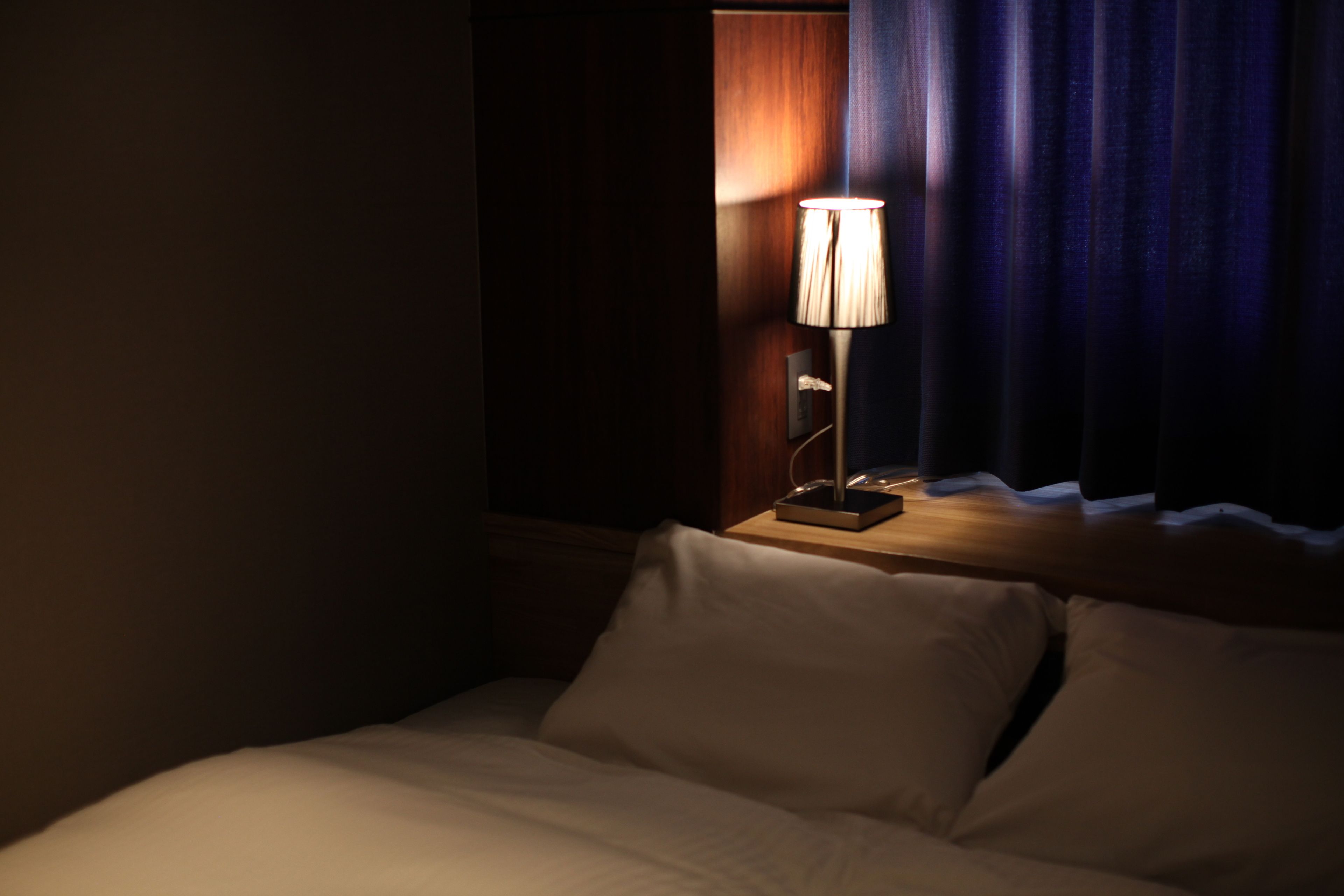 A hotel room with a bed, a nightstand with a lamp, and a window with curtains.