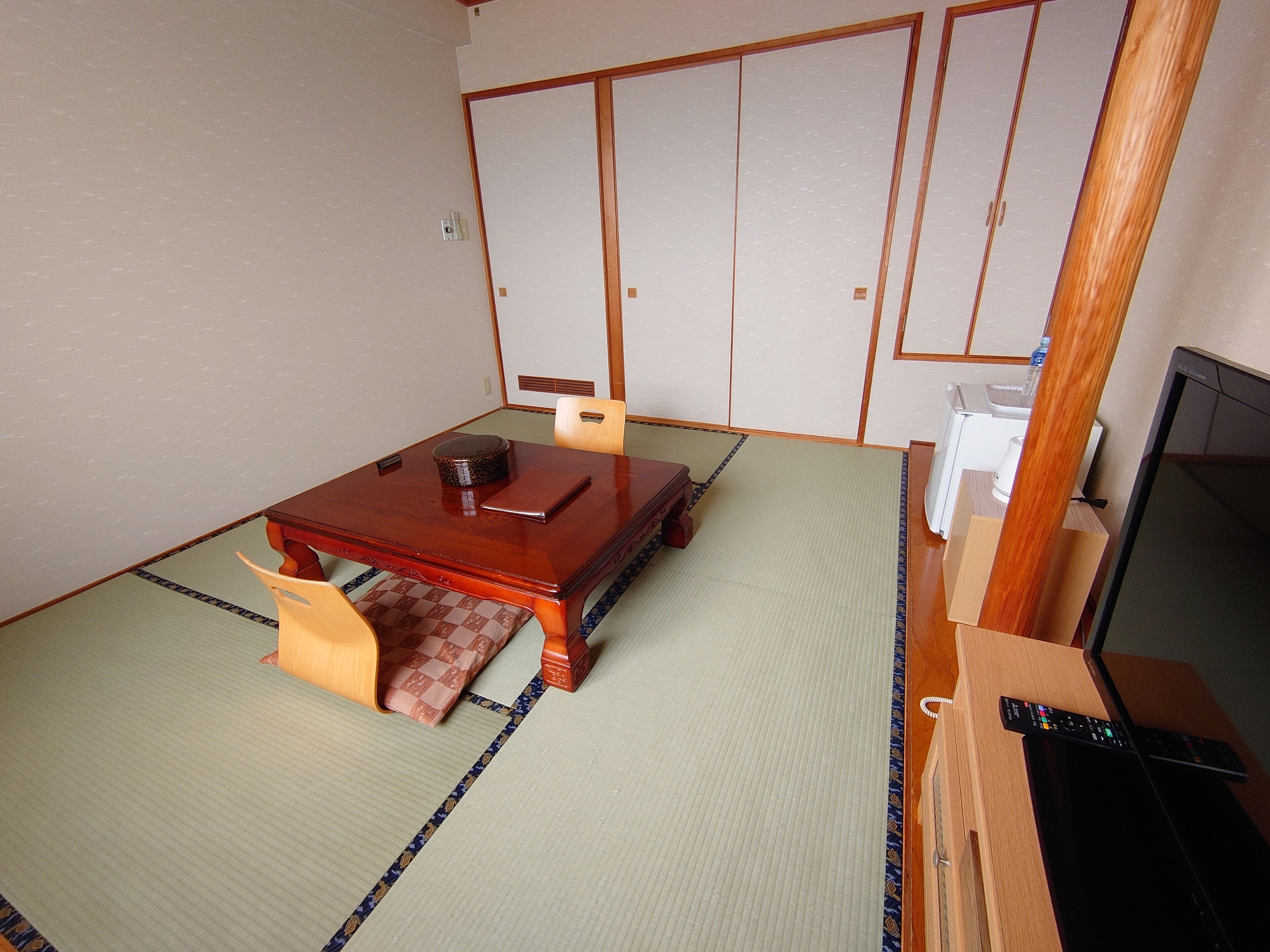 Habitació japonesa tradicional amb fons de tatami, una taula de fusta baixa, una cadira de tatami, un televisor i una porta corredissa.
