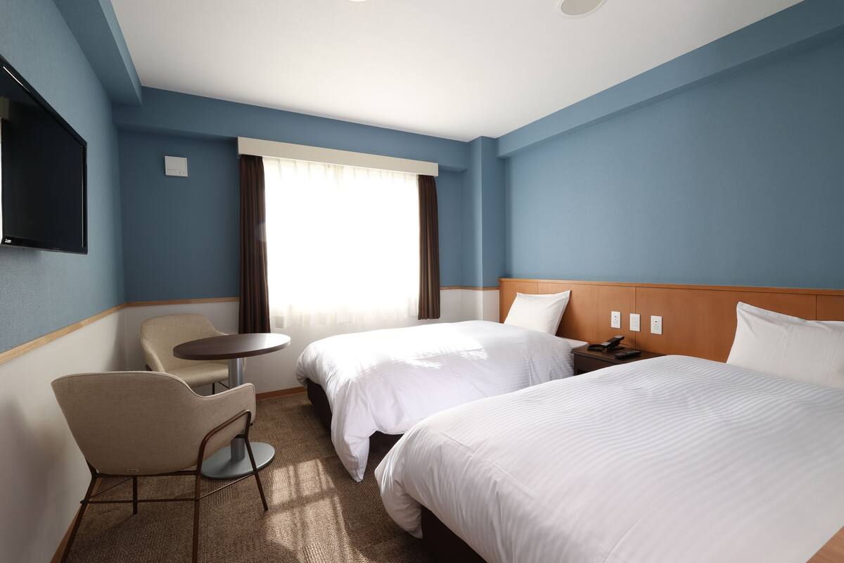 Une chambre d’hôtel avec deux lits, un bureau, une chaise et un téléviseur.