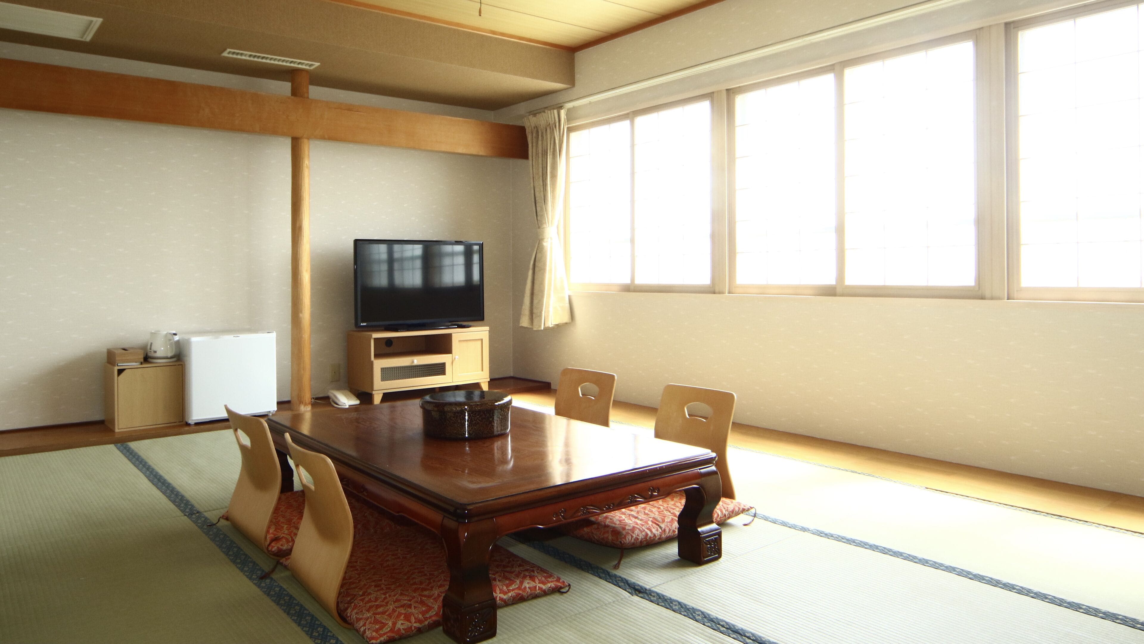 Une pièce de style japonais traditionnel, avec un sol recouvert de tatamis, une petite table en bois et un téléviseur posé sur un meuble.