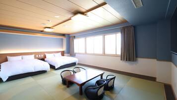 A hotel room with two beds, a dining table, chairs, tatami mats, and a large window with curtains.
