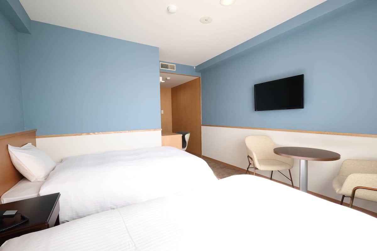 Une chambre d’hôtel avec deux lits, un bureau, une chaise, une télévision et une petite table.
