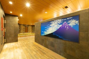 A hallway with a wooden ceiling, a large wall-mounted digital display of Mount Fuji, and a reception area with a stone wall and a wooden reception desk.