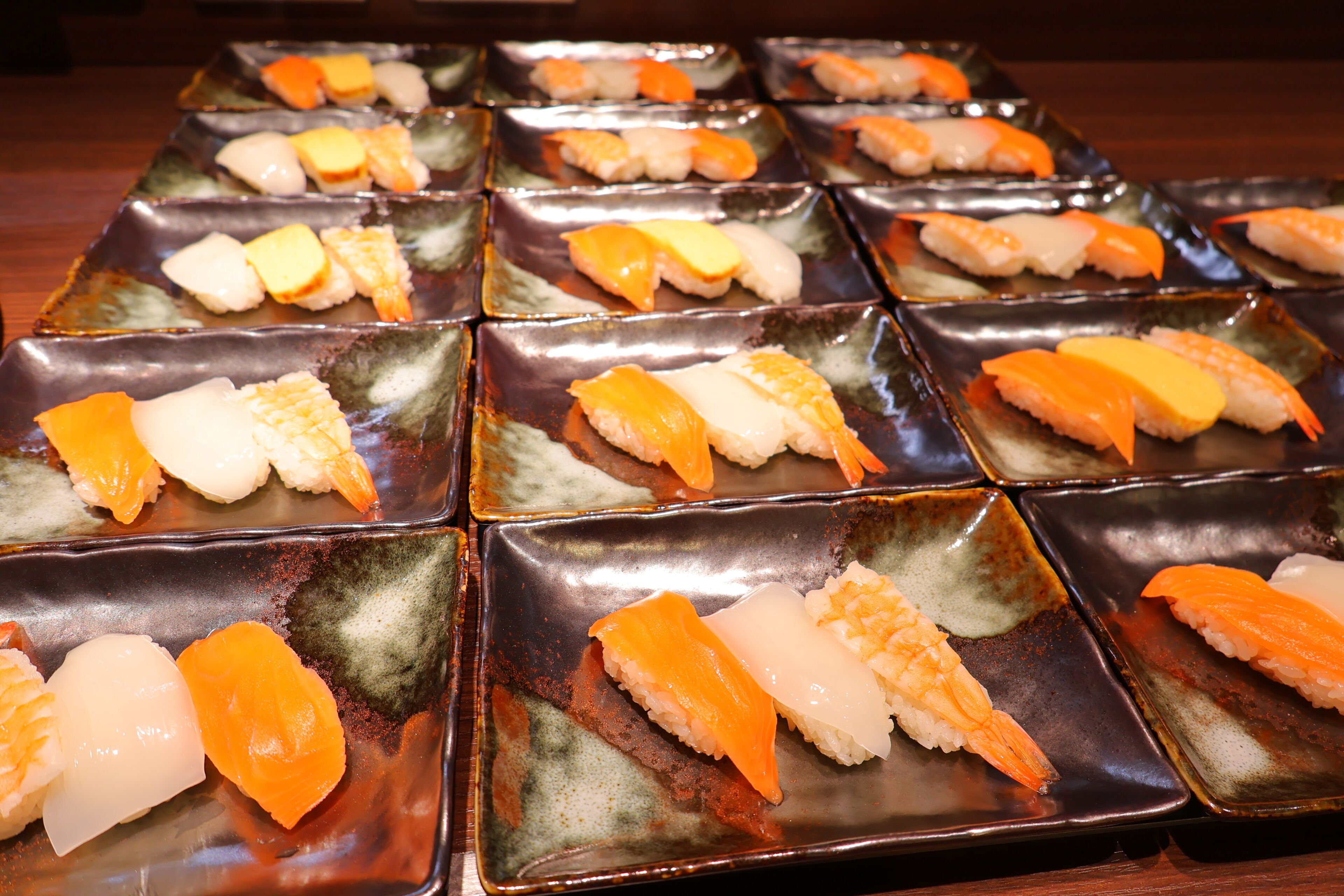 A selection of sushi arranged on square ceramic plates.