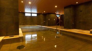 Una amplia piscina cubierta con suelo y paredes de azulejos, techo de madera y un pequeño ventanal.