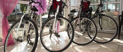 Three bicycles parked indoors with a pink curtain and a glass door in the background.