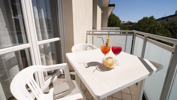 A balcony with a white table and chairs, two drinks, and a glass of juice. - Hotel Nuova Flavia (Lignano Sabbiadoro)