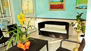 A room with a wicker sofa, a dining table with a vase of flowers, and a potted plant. - Hotel Nuova Flavia (Lignano Sabbiadoro)