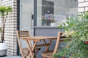 A wooden table and chairs outside a building with a brick wall and a window. - The Stay Simple (Seoul)